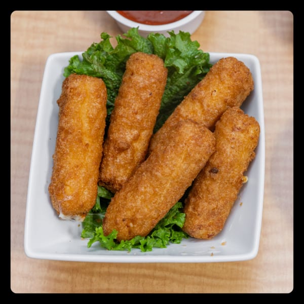 Five golden-brown mozzarella sticks on a bed of green lettuce, with a small bowl of red sauce.