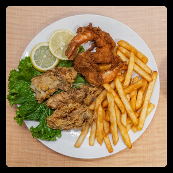 A white plate with fried chicken wings, fried shrimp, french fries, lettuce, and lemon slices.