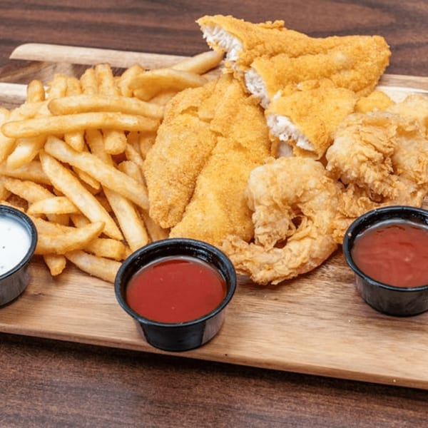 Fried fish fillets, shrimp, and french fries with dipping sauces on a wooden board.