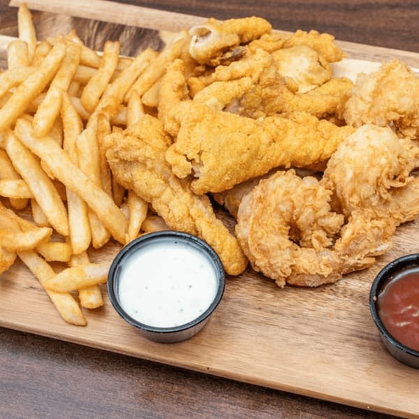 Golden fried fish, shrimp, and french fries with ranch and ketchup on a wooden board.