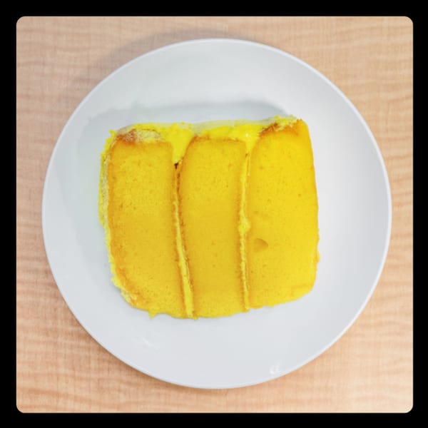 Slice of bright yellow cake with yellow frosting on a white plate.