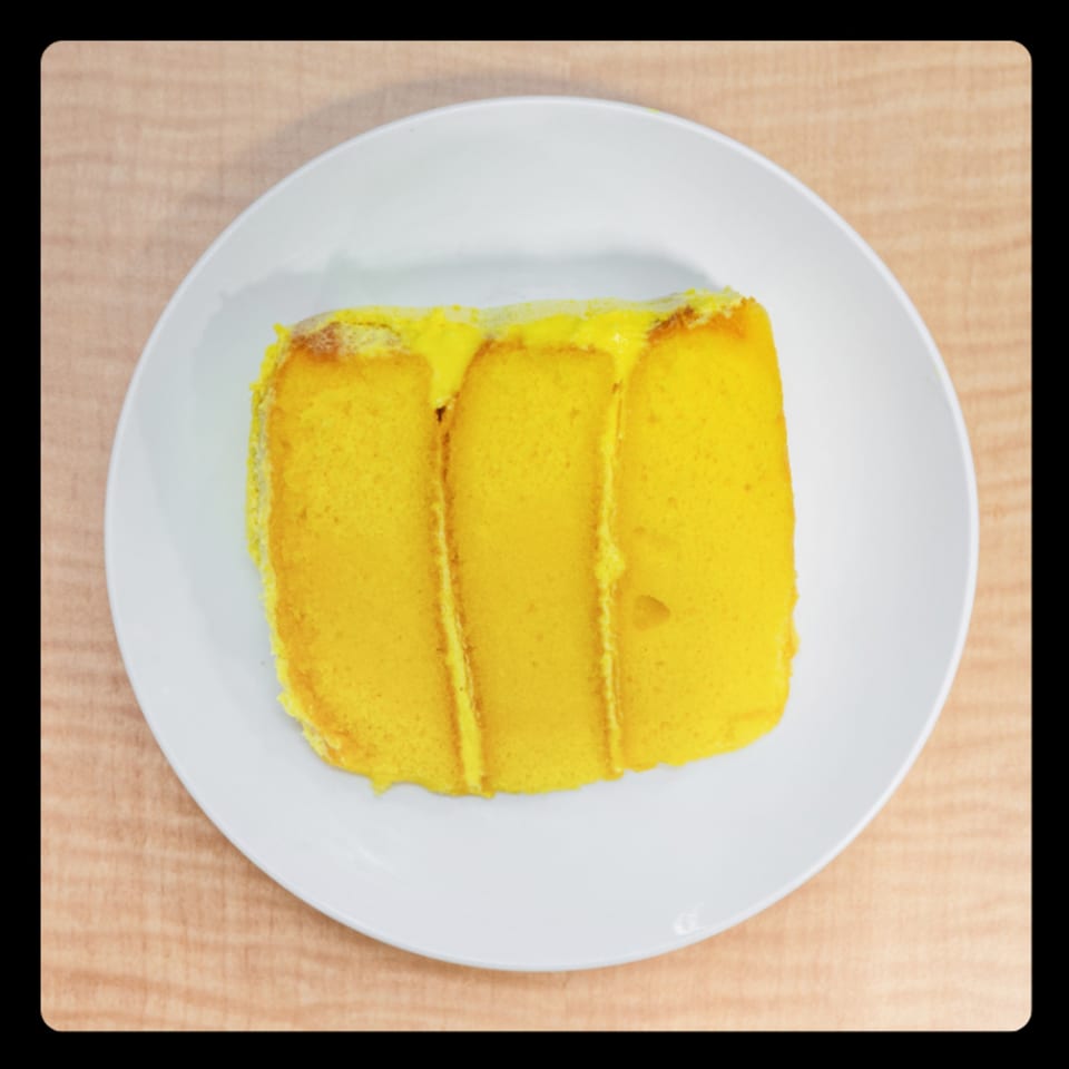 Slice of bright yellow cake with yellow frosting on a white plate.