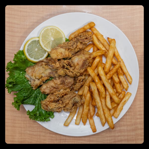 Crispy fried chicken wings with golden french fries, fresh lettuce, and lemon slices on a white plate.