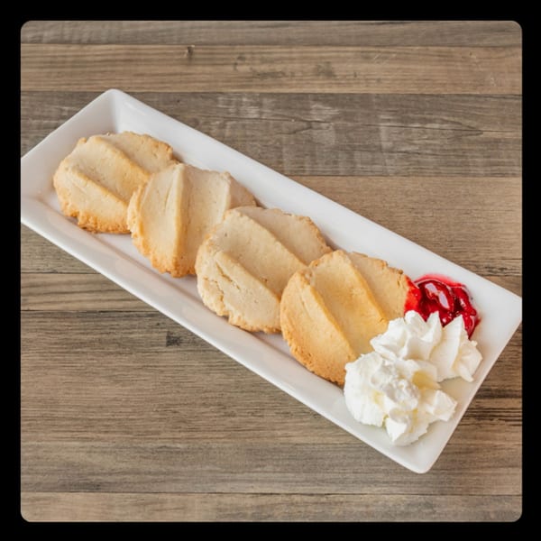 Shortbread cookies with whipped cream and cherry topping on a white rectangular plate.