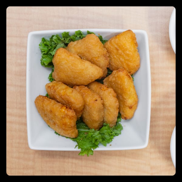 A white rectangular plate filled with golden-brown fried chicken wings on a bed of green lettuce.
