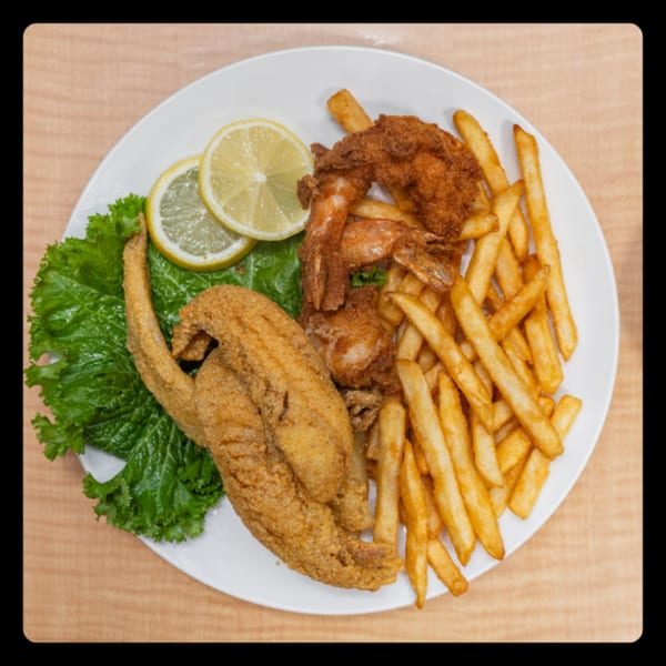 Fried fish, shrimp, and french fries with lemon slices and lettuce on a white plate.