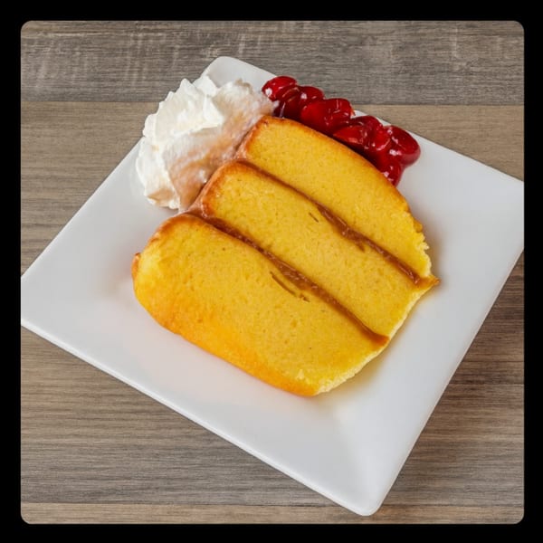 Three slices of golden pound cake with caramel drizzle, whipped cream, and cherry topping on a white plate.