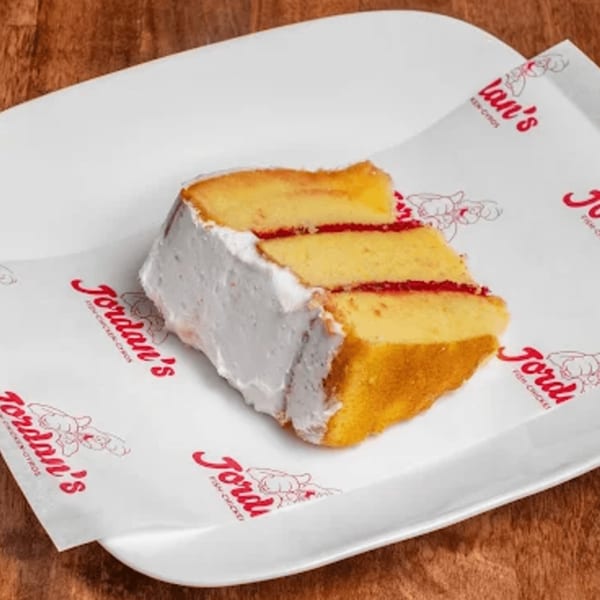 Slice of Jordan's vanilla cake with white frosting and red filling on branded wax paper.